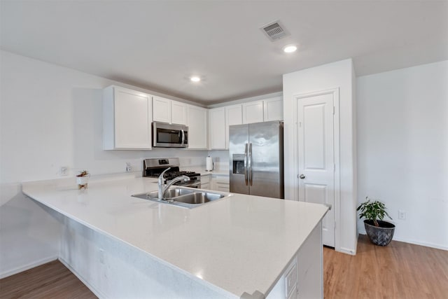 kitchen with light wood-style flooring, stainless steel appliances, a peninsula, a sink, and visible vents