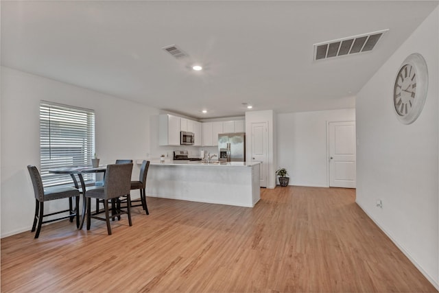 kitchen with a peninsula, appliances with stainless steel finishes, visible vents, and light wood-style floors