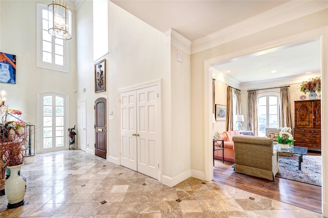 foyer entrance featuring ornamental molding, a towering ceiling, baseboards, and an inviting chandelier