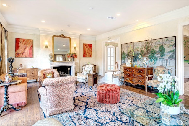 living room featuring crown molding, a fireplace, visible vents, and wood finished floors