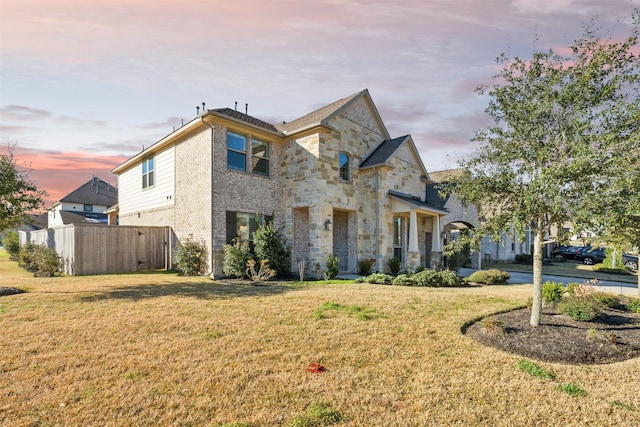 french provincial home featuring stone siding, brick siding, a yard, and fence