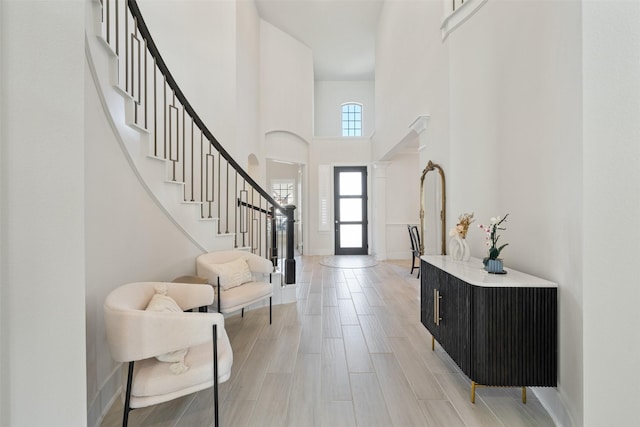 foyer with baseboards, a towering ceiling, stairway, ornate columns, and light wood-style floors