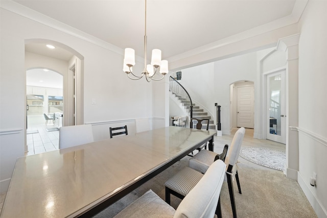 dining room featuring arched walkways, crown molding, a notable chandelier, baseboards, and stairs