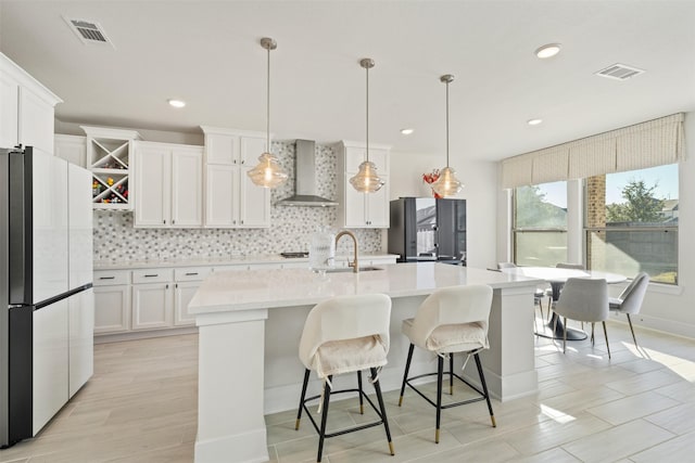 kitchen with wall chimney range hood, a sink, freestanding refrigerator, and tasteful backsplash