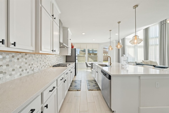 kitchen with stainless steel appliances, a sink, white cabinets, light countertops, and tasteful backsplash