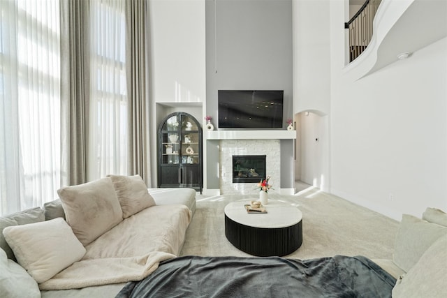 carpeted living area with arched walkways, a fireplace, and a high ceiling