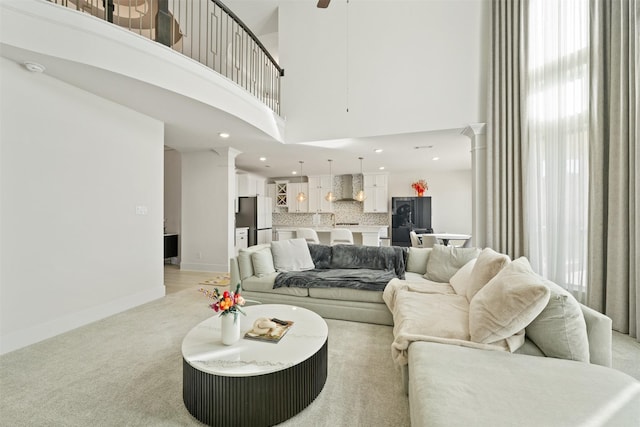 living area featuring a towering ceiling, decorative columns, baseboards, and light colored carpet