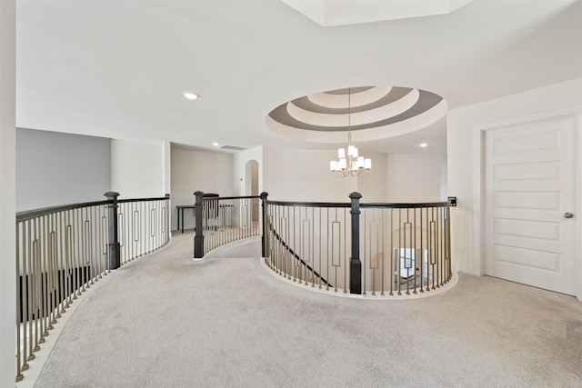 corridor with carpet floors, a tray ceiling, a chandelier, and an upstairs landing