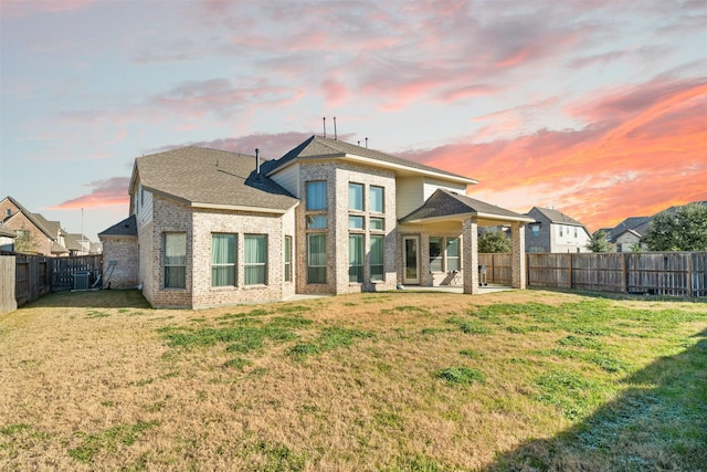 rear view of house with a yard, brick siding, central AC unit, and a fenced backyard