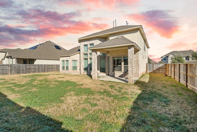 back of house with a patio, brick siding, a lawn, and a fenced backyard