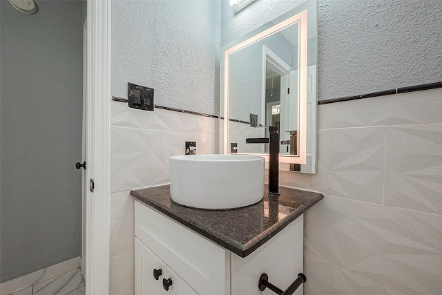 bathroom with marble finish floor, a textured wall, tile walls, and vanity