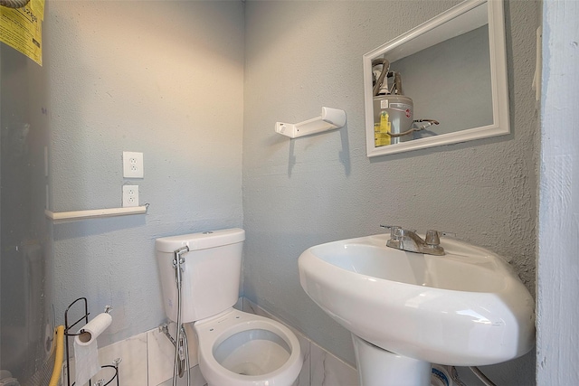 half bathroom featuring toilet, a sink, and a textured wall