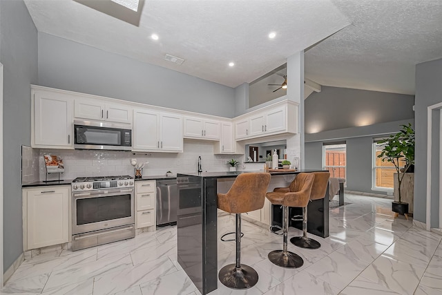 kitchen featuring marble finish floor, appliances with stainless steel finishes, tasteful backsplash, dark countertops, and a kitchen bar