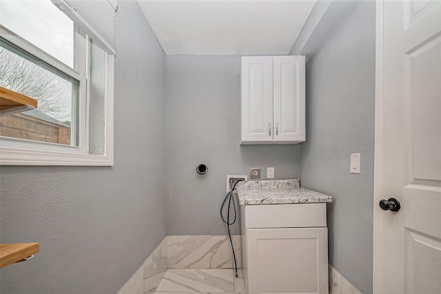 laundry room featuring marble finish floor, washer hookup, cabinet space, and a textured wall