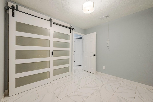 empty room with marble finish floor, a barn door, visible vents, and a textured ceiling