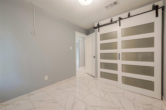 unfurnished room with marble finish floor, visible vents, a textured ceiling, and a barn door