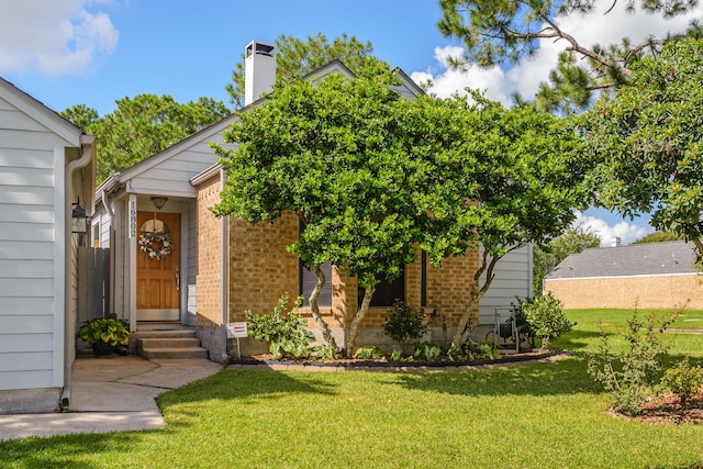 obstructed view of property with a chimney, a front lawn, and brick siding