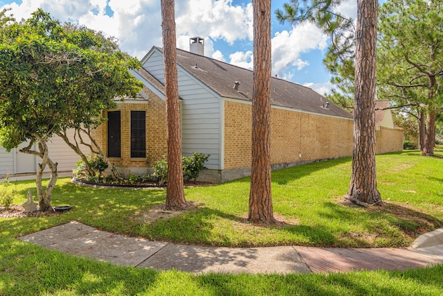 view of side of property with brick siding, a shingled roof, a chimney, and a yard