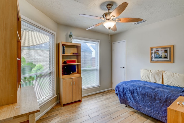 bedroom with a textured ceiling, a ceiling fan, visible vents, baseboards, and light wood finished floors