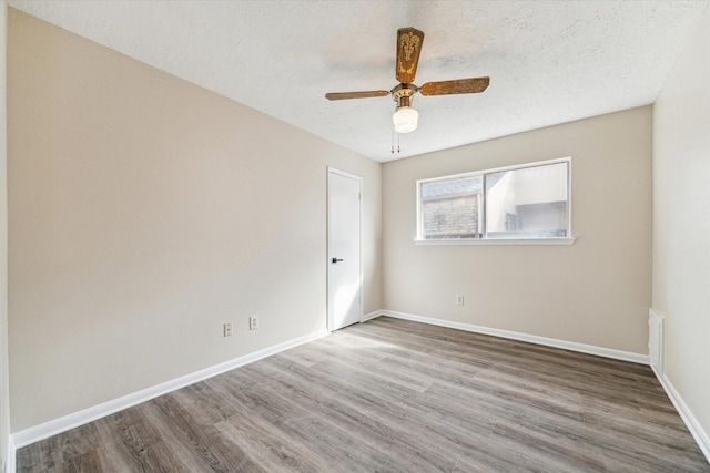 empty room featuring a textured ceiling, baseboards, and wood finished floors