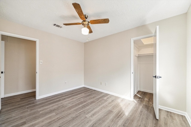 unfurnished bedroom featuring visible vents, a walk in closet, wood finished floors, a closet, and a textured ceiling