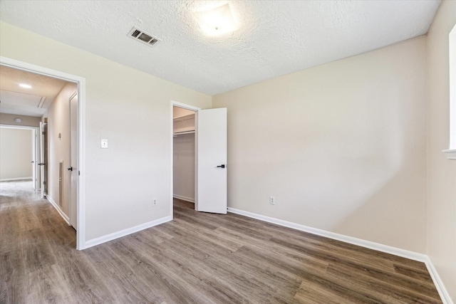 unfurnished bedroom with visible vents, a textured ceiling, baseboards, and wood finished floors