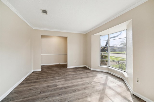 unfurnished room with visible vents, baseboards, wood finished floors, and ornamental molding