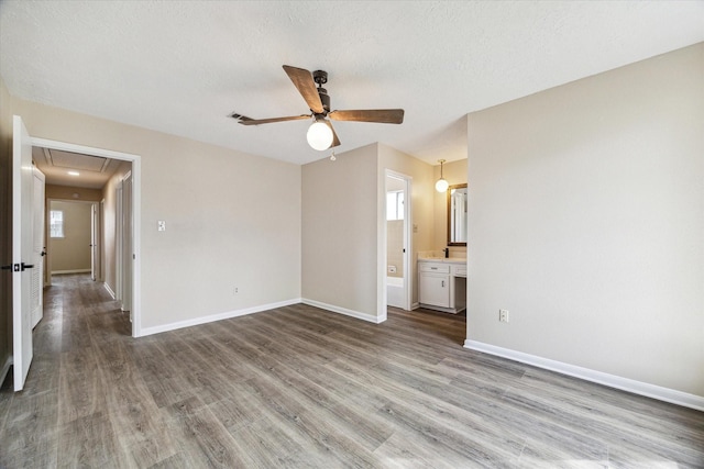 unfurnished bedroom featuring baseboards, attic access, wood finished floors, a textured ceiling, and ensuite bath