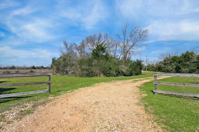 exterior space featuring driveway, fence, a lawn, and a rural view