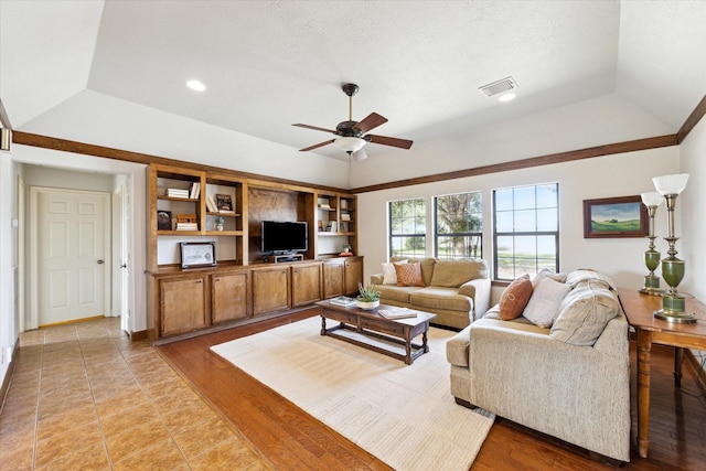 living area with light wood-style flooring, a tray ceiling, vaulted ceiling, and a ceiling fan