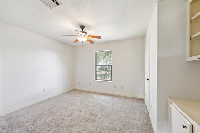 spare room with a textured ceiling, light carpet, visible vents, baseboards, and a ceiling fan