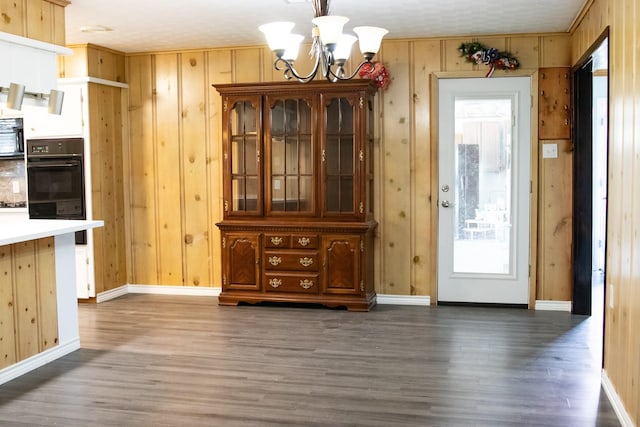 unfurnished dining area with a chandelier, wooden walls, baseboards, and wood finished floors