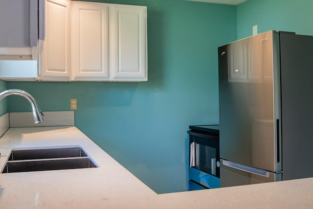 kitchen featuring light countertops, a sink, freestanding refrigerator, and white cabinetry