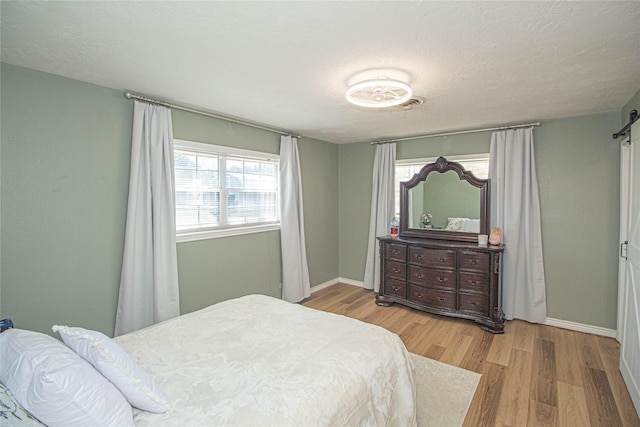 bedroom featuring a textured ceiling, a barn door, wood finished floors, and baseboards