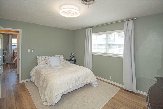 bedroom featuring light wood-style flooring, a textured ceiling, visible vents, and baseboards