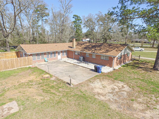 back of house featuring a lawn, concrete driveway, fence, central air condition unit, and brick siding