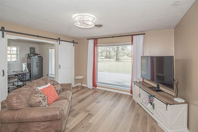 living room with light wood-type flooring, a healthy amount of sunlight, a textured ceiling, and a barn door