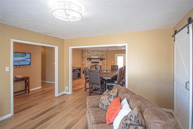 living room with a textured ceiling, a barn door, baseboards, and light wood-style floors