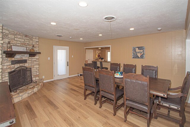 dining room featuring a stone fireplace, visible vents, light wood-style flooring, and a textured ceiling