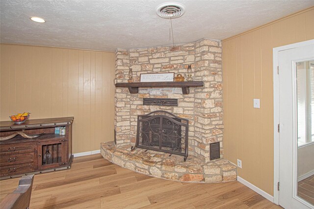 living room featuring visible vents, a fireplace, a textured ceiling, and wood finished floors