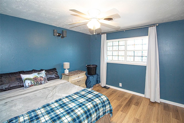 bedroom with baseboards, visible vents, a ceiling fan, wood finished floors, and a textured ceiling