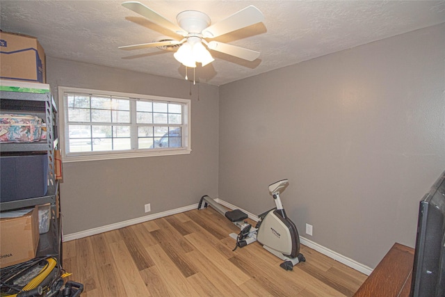 exercise area featuring light wood-type flooring, baseboards, and a textured ceiling