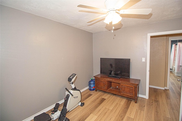 workout area featuring light wood-style floors, ceiling fan, a textured ceiling, and baseboards