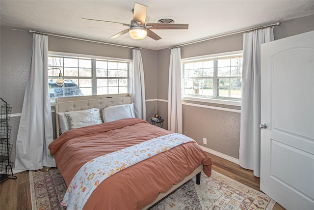 bedroom with multiple windows, a textured wall, and wood finished floors