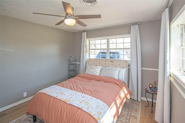 bedroom with a textured ceiling, ceiling fan, wood finished floors, visible vents, and baseboards