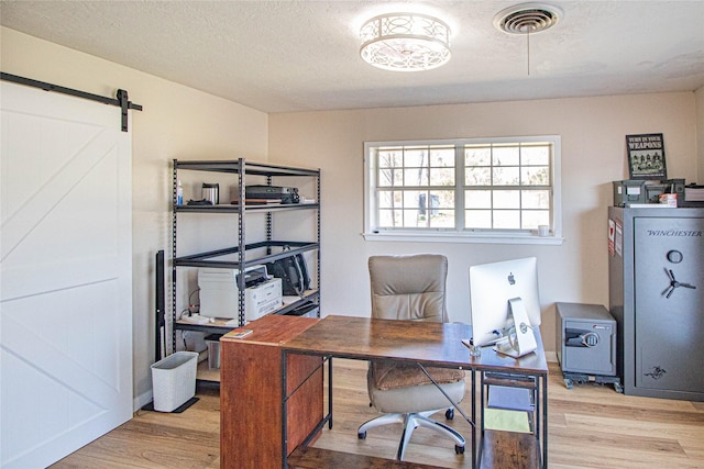 home office with a textured ceiling, a barn door, light wood-style flooring, and visible vents