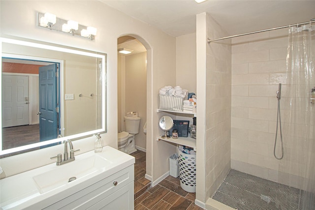 full bathroom featuring wood tiled floor, a tile shower, vanity, and toilet