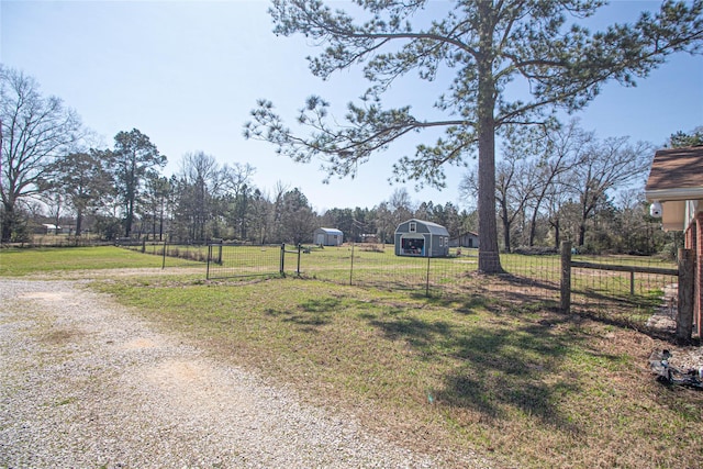 view of yard featuring driveway, a rural view, an outdoor structure, and fence