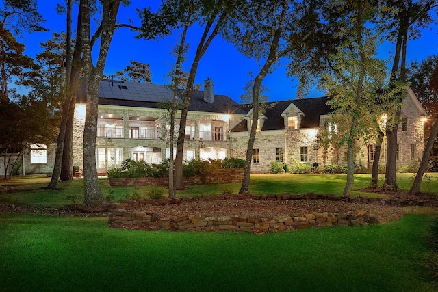 view of front of house with solar panels, a balcony, stone siding, a chimney, and a front yard