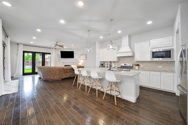 kitchen with custom exhaust hood, a fireplace, appliances with stainless steel finishes, open floor plan, and backsplash